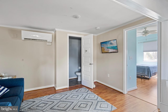 sitting room with crown molding, light wood finished floors, baseboards, and a wall mounted air conditioner