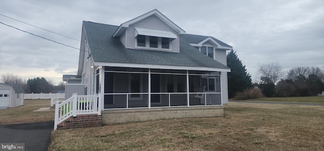 view of front of property featuring a lawn, a shingled roof, and a sunroom