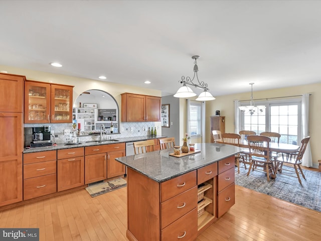 kitchen with light wood-type flooring, brown cabinets, a kitchen island, and a sink