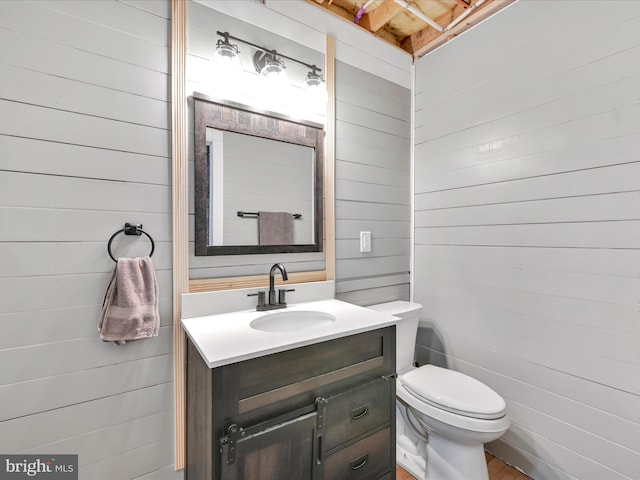 half bath with toilet, vanity, and wooden walls