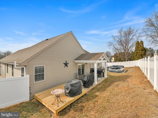 back of house with a shingled roof, a fenced backyard, a yard, and a deck