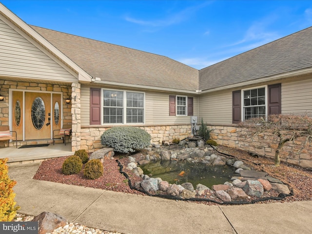 view of exterior entry featuring stone siding and roof with shingles