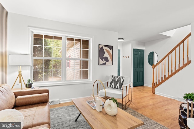 living room featuring baseboards, a healthy amount of sunlight, stairway, and light wood finished floors