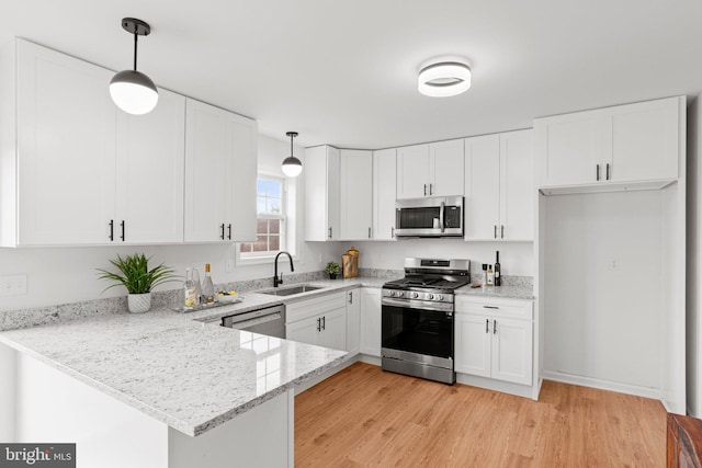 kitchen with a peninsula, appliances with stainless steel finishes, a sink, and white cabinets