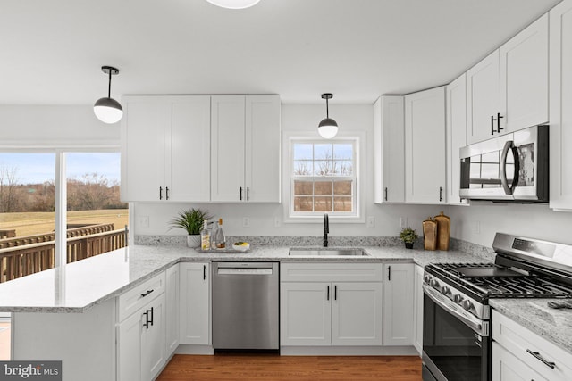 kitchen with a peninsula, appliances with stainless steel finishes, a sink, and white cabinets