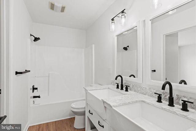 bathroom featuring visible vents, toilet, wood finished floors,  shower combination, and a sink