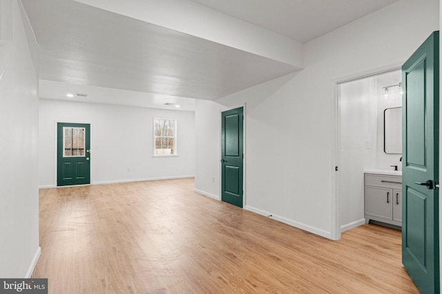 interior space with light wood-type flooring, a sink, and baseboards