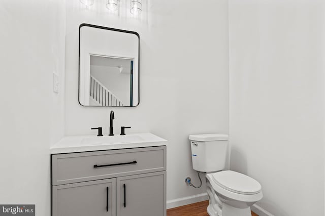 half bath with toilet, baseboards, wood finished floors, and vanity