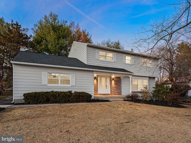 view of front facade featuring a front yard, brick siding, and roof with shingles