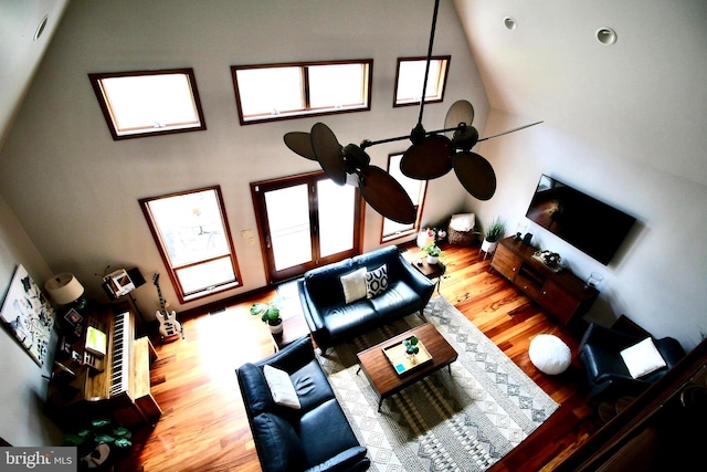 living area with a ceiling fan, wood finished floors, and a towering ceiling
