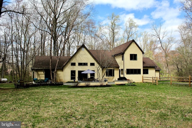 rear view of house featuring a yard, fence, and stucco siding