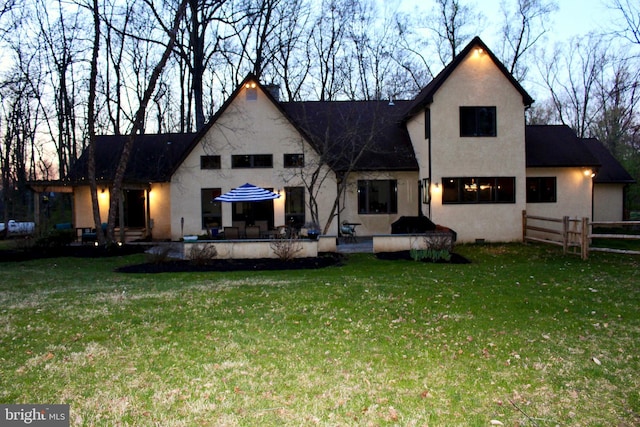 rear view of house featuring a lawn, a patio area, stucco siding, and fence