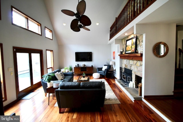 living room with plenty of natural light, a ceiling fan, a stone fireplace, and high vaulted ceiling