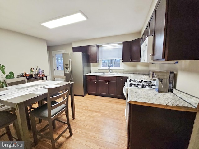 kitchen featuring white appliances, a sink, light countertops, dark brown cabinets, and light wood finished floors