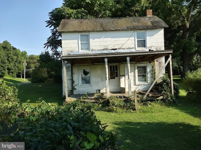 view of front of house featuring covered porch, a front lawn, and a chimney