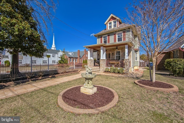 american foursquare style home with covered porch, stone siding, a front yard, and fence