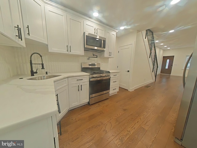 kitchen with tasteful backsplash, light wood-style flooring, appliances with stainless steel finishes, white cabinetry, and a sink