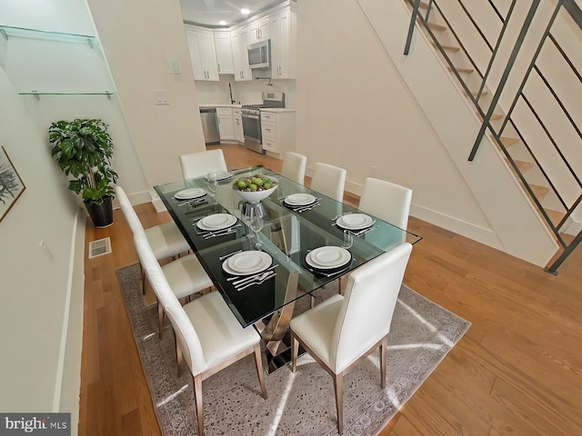 dining area with stairs, light wood finished floors, visible vents, and baseboards