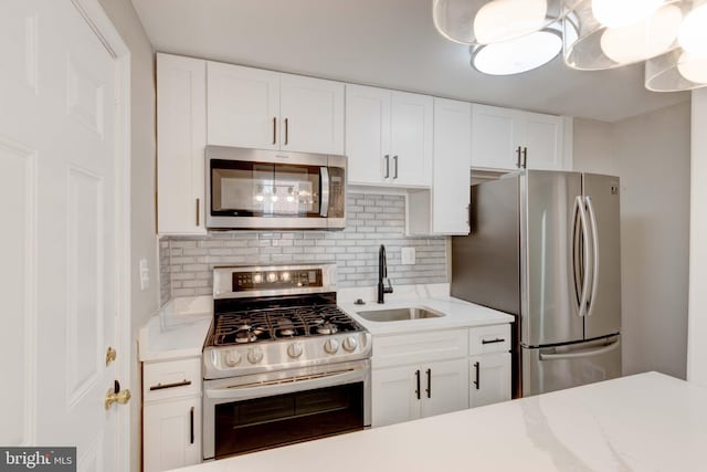 kitchen with stainless steel appliances, decorative backsplash, white cabinets, a sink, and light stone countertops