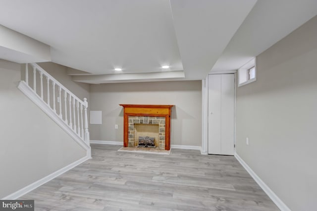 unfurnished living room featuring a stone fireplace, recessed lighting, wood finished floors, baseboards, and stairway