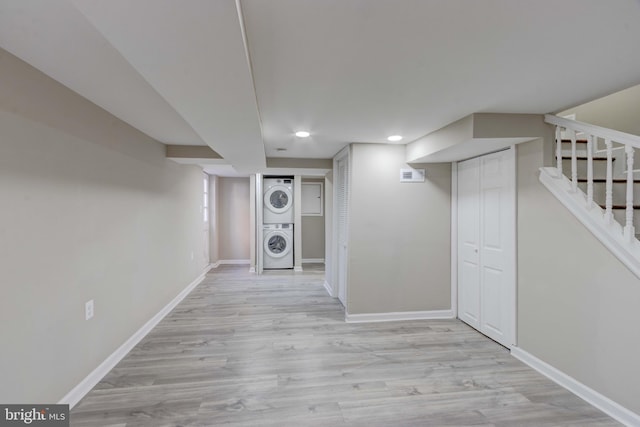 finished below grade area featuring stacked washer and clothes dryer, recessed lighting, stairway, wood finished floors, and baseboards