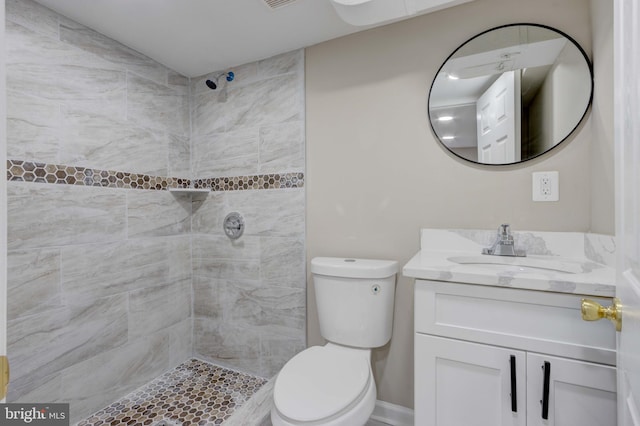 bathroom with toilet, a tile shower, and vanity