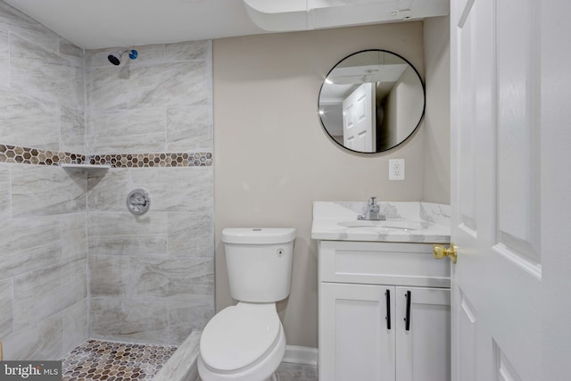 full bathroom featuring toilet, tiled shower, vanity, and baseboards