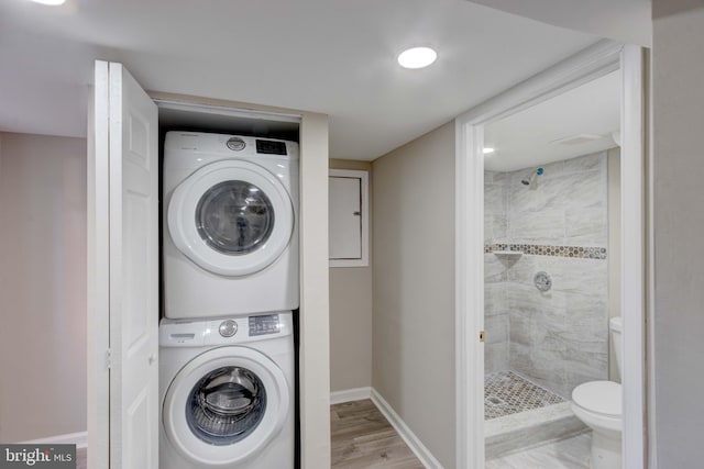 laundry room with stacked washer and clothes dryer, baseboards, and wood finished floors