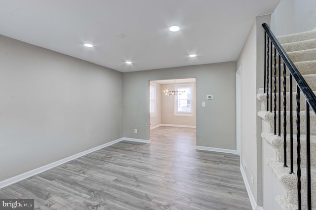 spare room featuring baseboards, stairway, wood finished floors, a notable chandelier, and recessed lighting