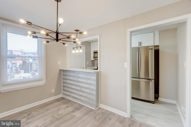 kitchen with white cabinetry, baseboards, light wood-style floors, appliances with stainless steel finishes, and pendant lighting