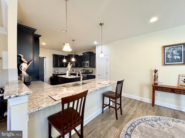 kitchen featuring a kitchen bar, light wood-style flooring, a sink, stainless steel appliances, and a peninsula