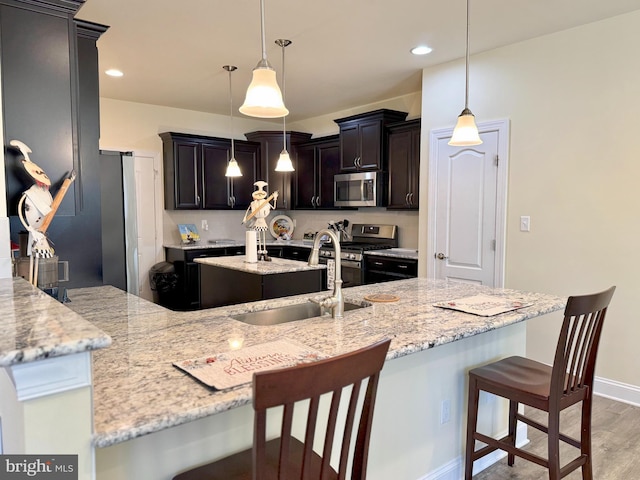 kitchen with a center island with sink, a sink, light wood-style floors, appliances with stainless steel finishes, and a kitchen breakfast bar