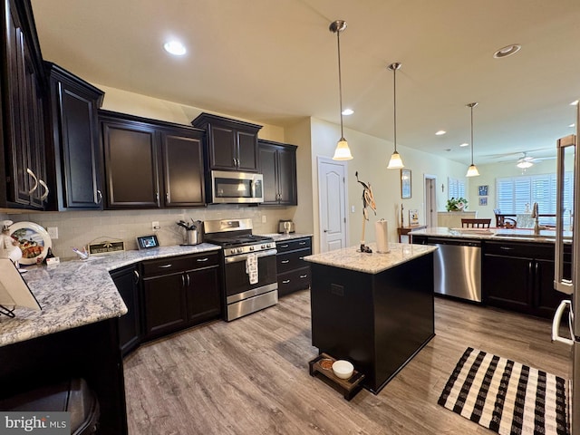 kitchen featuring a sink, decorative backsplash, stainless steel appliances, light wood-type flooring, and a center island