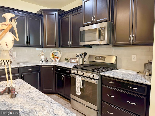 kitchen featuring light stone counters, tasteful backsplash, dark brown cabinets, and stainless steel appliances