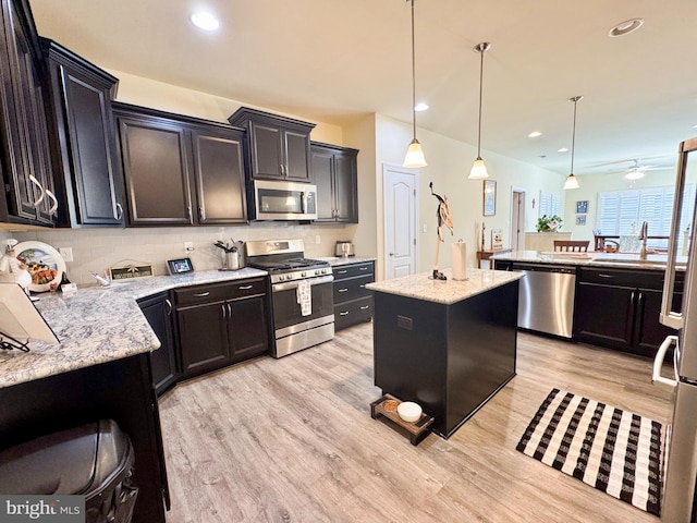 kitchen featuring light wood finished floors, backsplash, decorative light fixtures, stainless steel appliances, and a sink