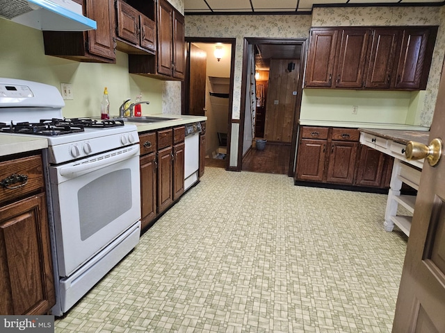 kitchen with light countertops, a sink, white appliances, under cabinet range hood, and wallpapered walls