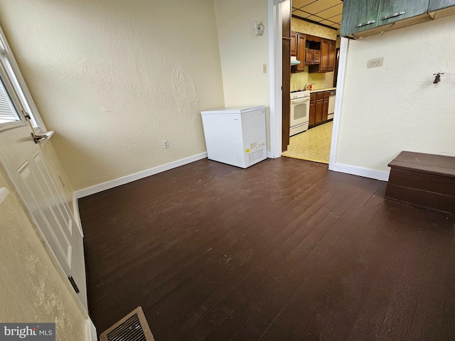 spare room featuring baseboards, visible vents, dark wood-type flooring, and a textured wall