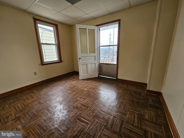 unfurnished room with baseboards, a paneled ceiling, and a healthy amount of sunlight