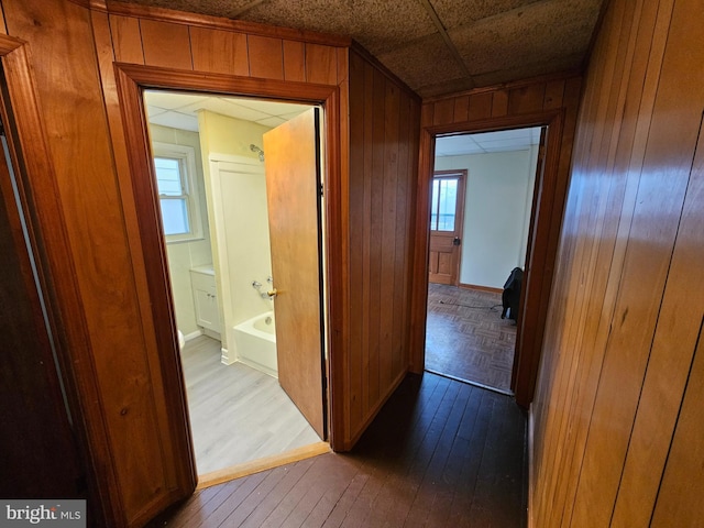 corridor with dark wood-style floors, baseboards, and wooden walls