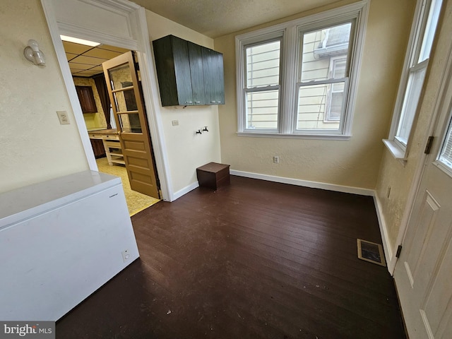 empty room featuring dark wood-style flooring, a drop ceiling, visible vents, and baseboards