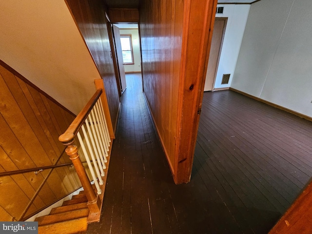 hallway with wooden walls, visible vents, and hardwood / wood-style floors