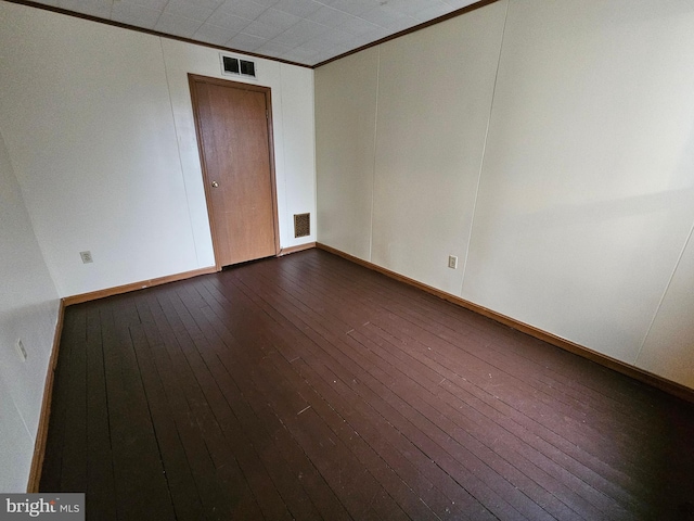 empty room with baseboards, visible vents, dark wood-type flooring, and crown molding