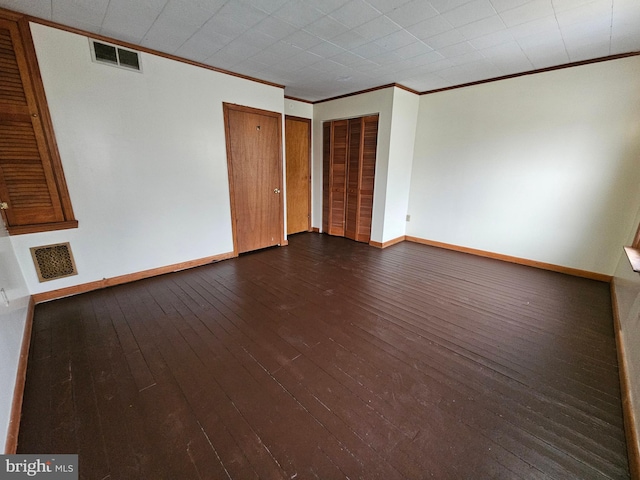 spare room featuring ornamental molding, dark wood-type flooring, visible vents, and baseboards