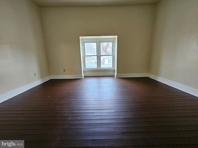 spare room with dark wood-type flooring and baseboards