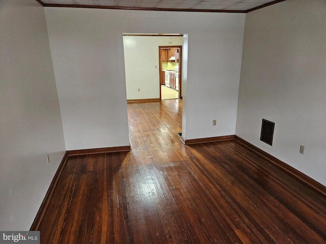 empty room with ornamental molding, wood-type flooring, visible vents, and baseboards