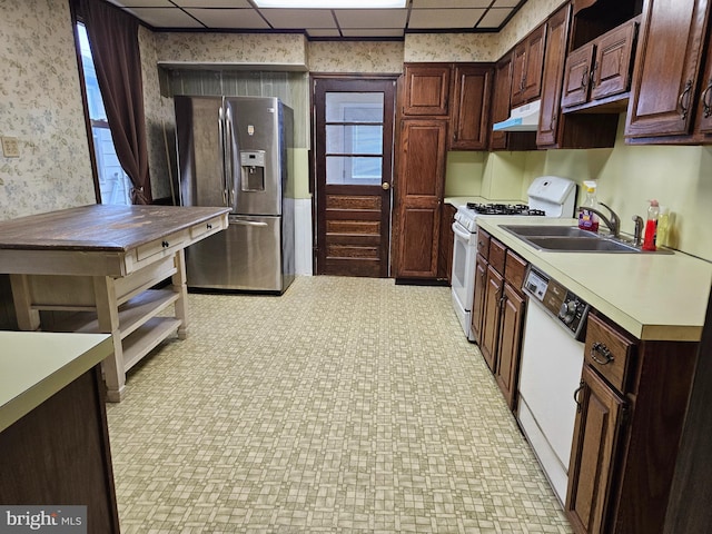 kitchen with under cabinet range hood, white appliances, a sink, light floors, and wallpapered walls