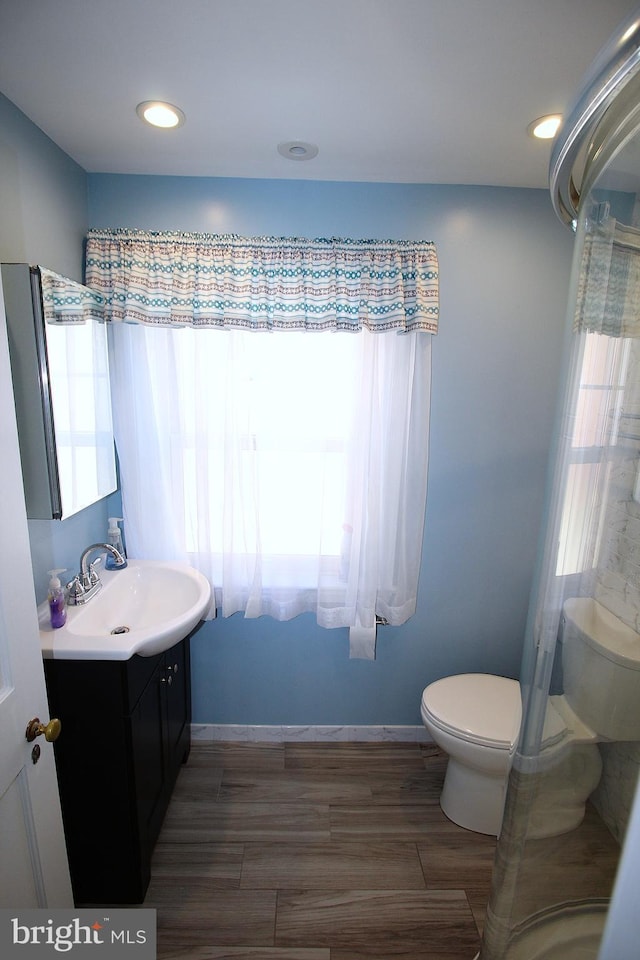 bathroom with toilet, plenty of natural light, baseboards, and vanity