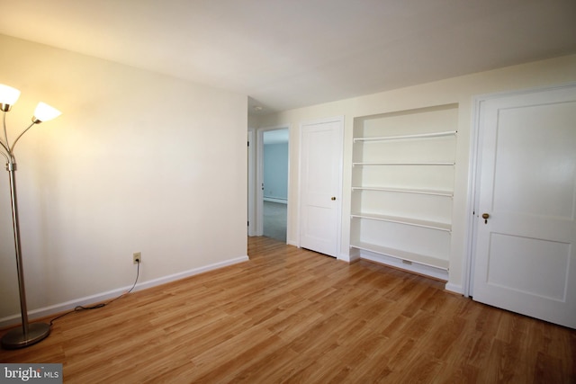 unfurnished bedroom with a baseboard heating unit, a closet, light wood-style flooring, and baseboards