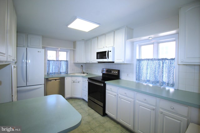 kitchen featuring appliances with stainless steel finishes, a sink, white cabinetry, and tasteful backsplash