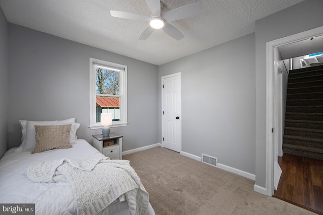 bedroom featuring visible vents, a textured ceiling, carpet floors, baseboards, and ceiling fan